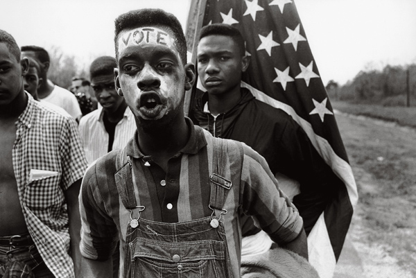 Bruce Davidson, Led by Martin Luther King Jr., a group of civil rights demonstrators march from Selma to Montgomery to fight for black suffrage. A young African American man with the word "VOTE" on his forehead, Alabama, 1965 © the artist/Magnum Photos