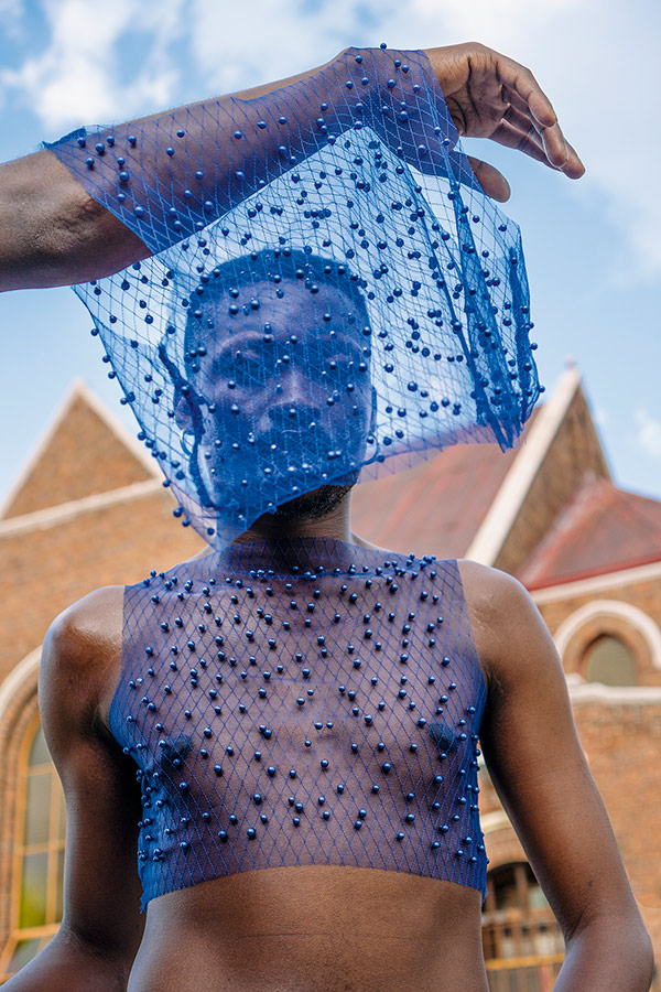 Jamal Nxedlana, FAKA Portrait, Johannesburg, 2019. Person in a mesh crop top. An arm above them drapes mesh in front of their face.