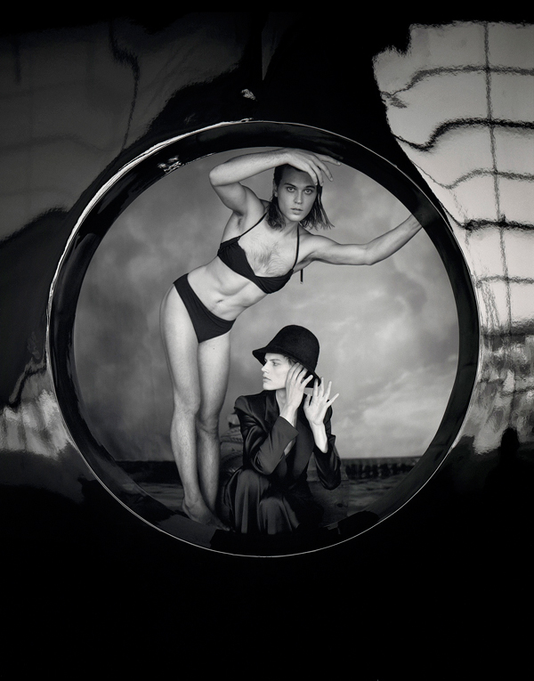 Black-and-white studio photograph of two people, one wearing a black bikini