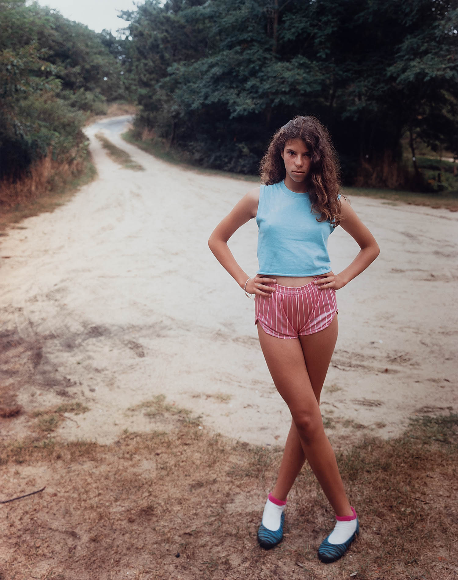 A woman stands in the middle of a dirt road with her hands on her hips