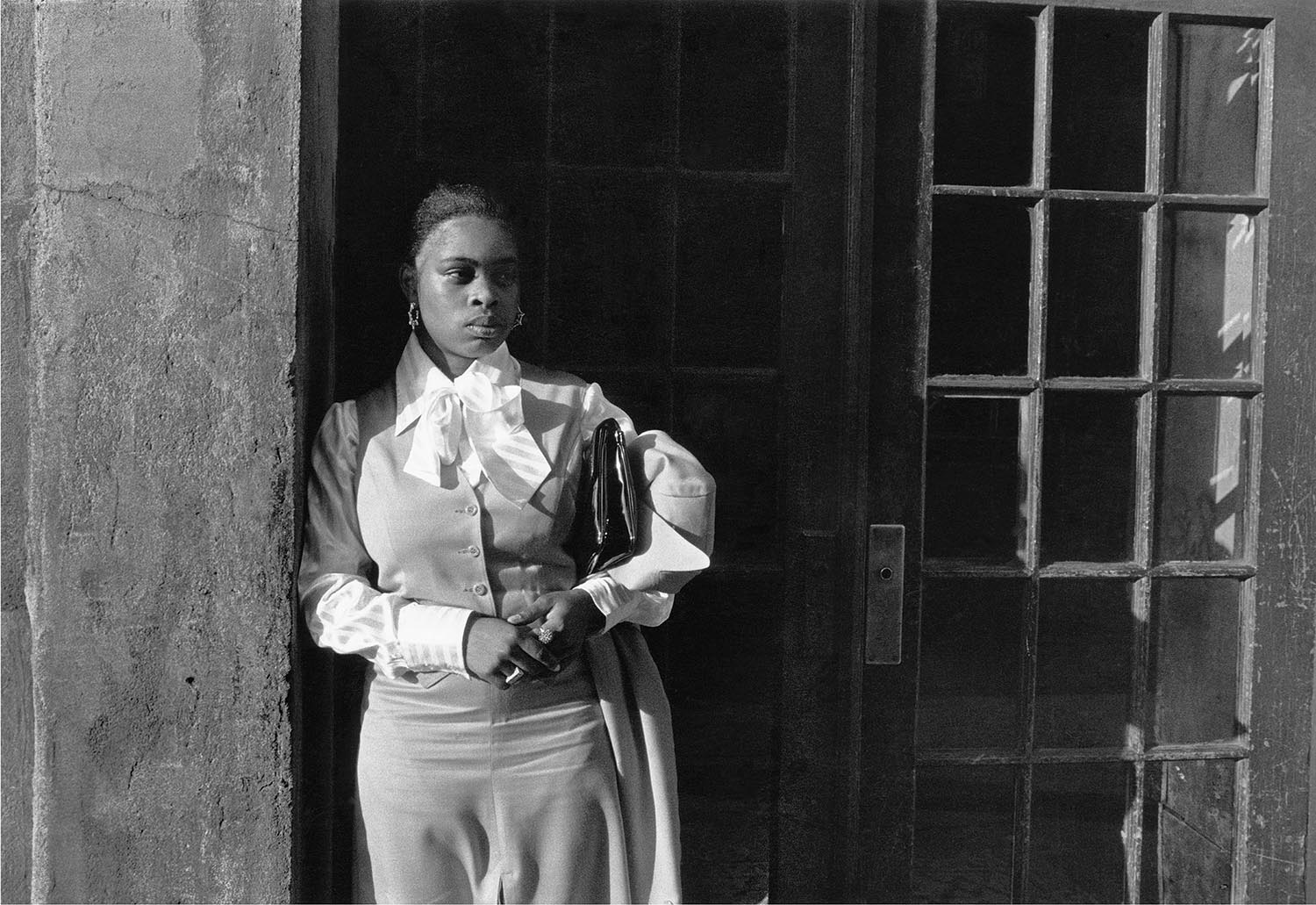 A black and white photograph of a woman waiting in a doorway