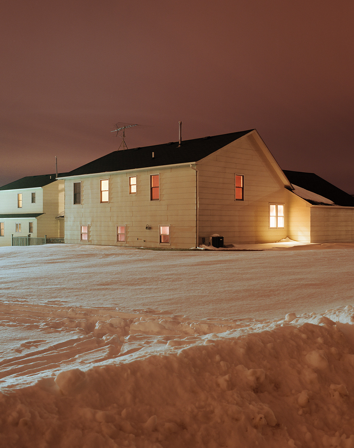 A white house at night, surrounded by snow, with light coming from the windows