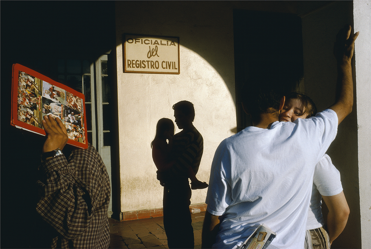 The shadow of a man holding a child is illuminated on a wall, with a couple embracing in the foreground