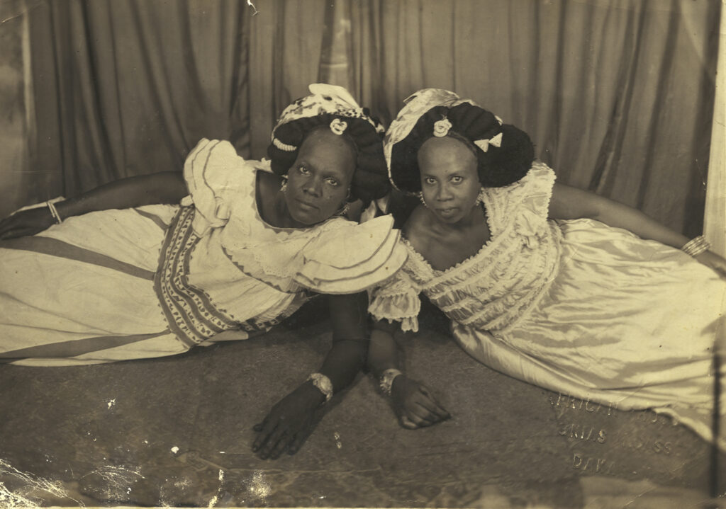 Black and white photograph of two reclining Senegalese women in white dresses