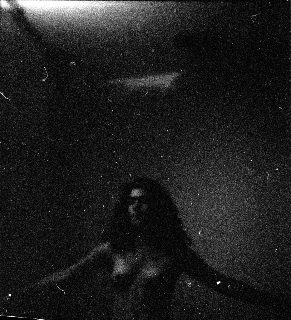 A black and white photograph of a nude woman in a dark room