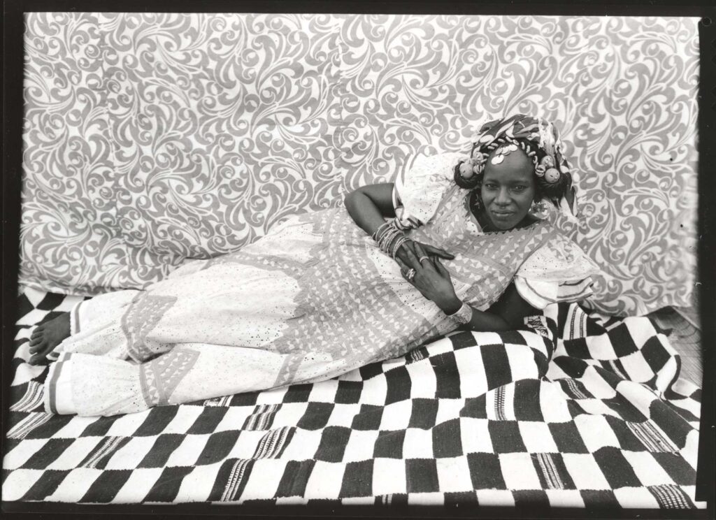 Black and white portrait of a Black woman reclining against a patterned backdrop