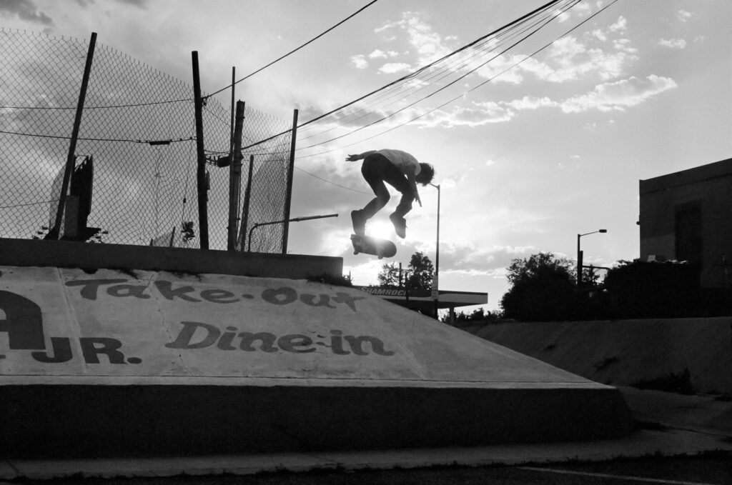 A black and white photograph of a skateboarder just barely obscuring the sun as he gains lift.