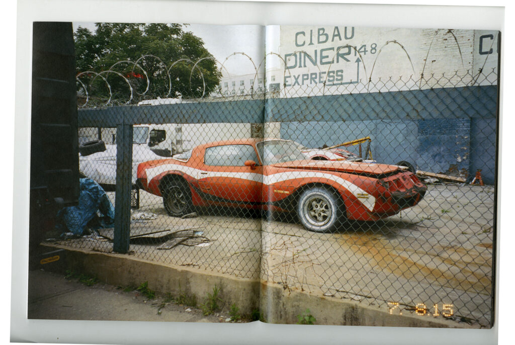 An orange car sits behind a chainlink fence topped by coiled barbed wire.