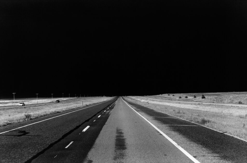A black and white photo of an empty highway stretching into the distance.