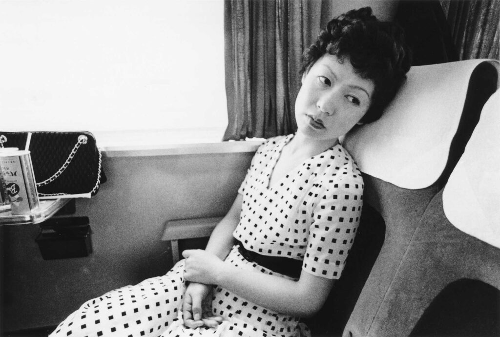 Black and white photograph of a Japanese woman in a patterned dress on a train