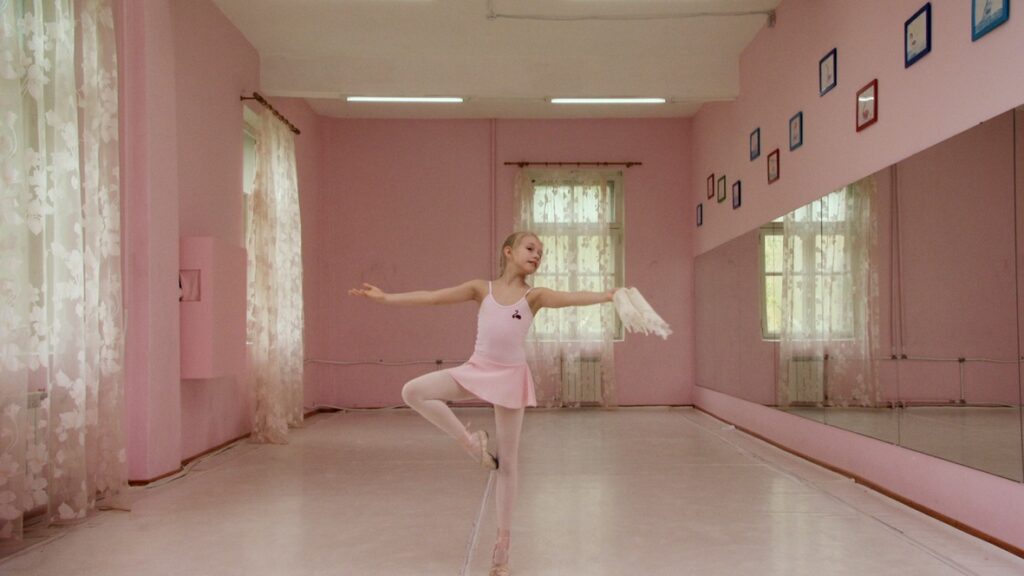 Video still of a young girl in a pink dress in a ballet pose