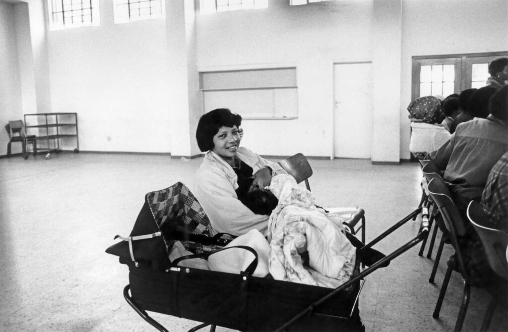 Black and white photograph of a South African woman sitting in a meeting hall