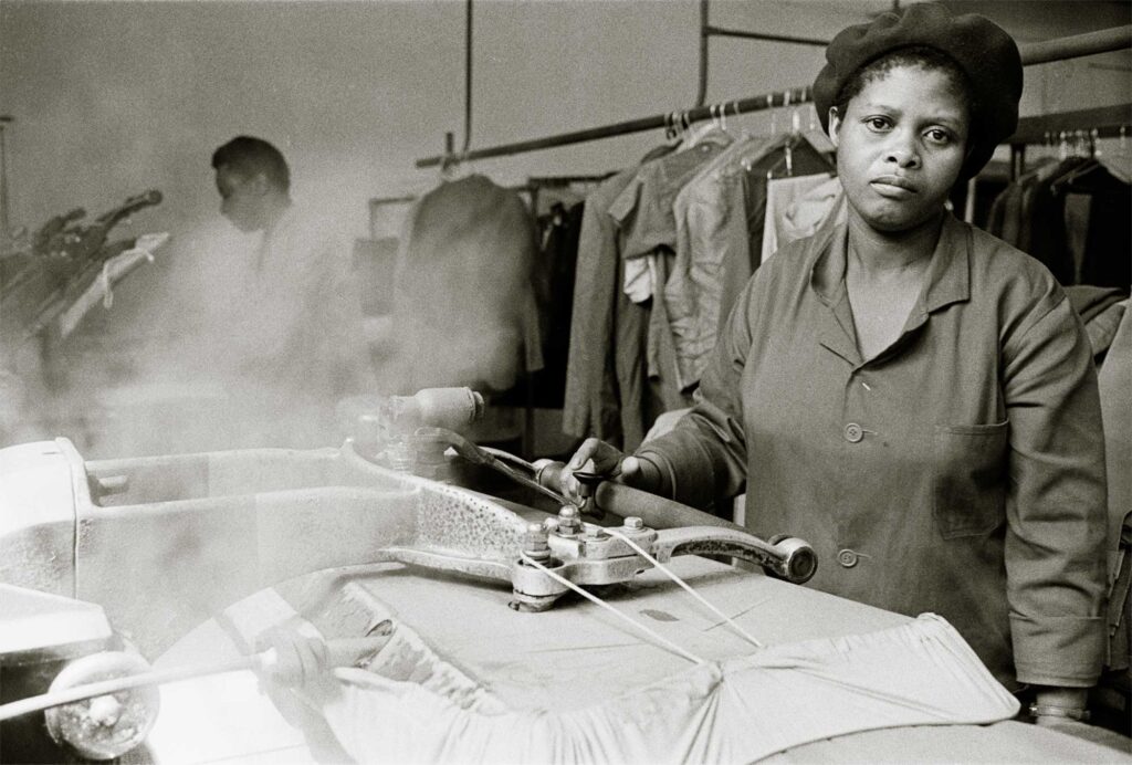 Black and white photograph of a South African woman working a laundry press