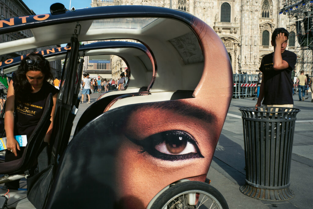 A small passenger cart on the streets of Milan with a thickly lined eye printed on the vehicle.