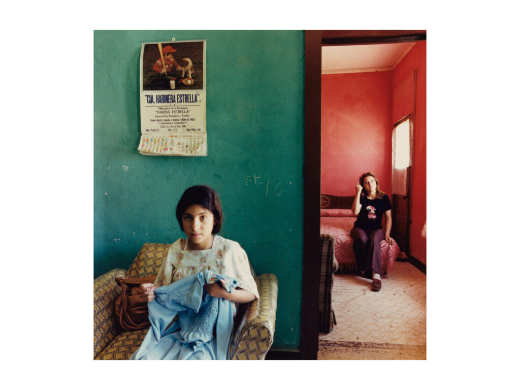 A young girl and young women sit in two rooms, one green, one red.