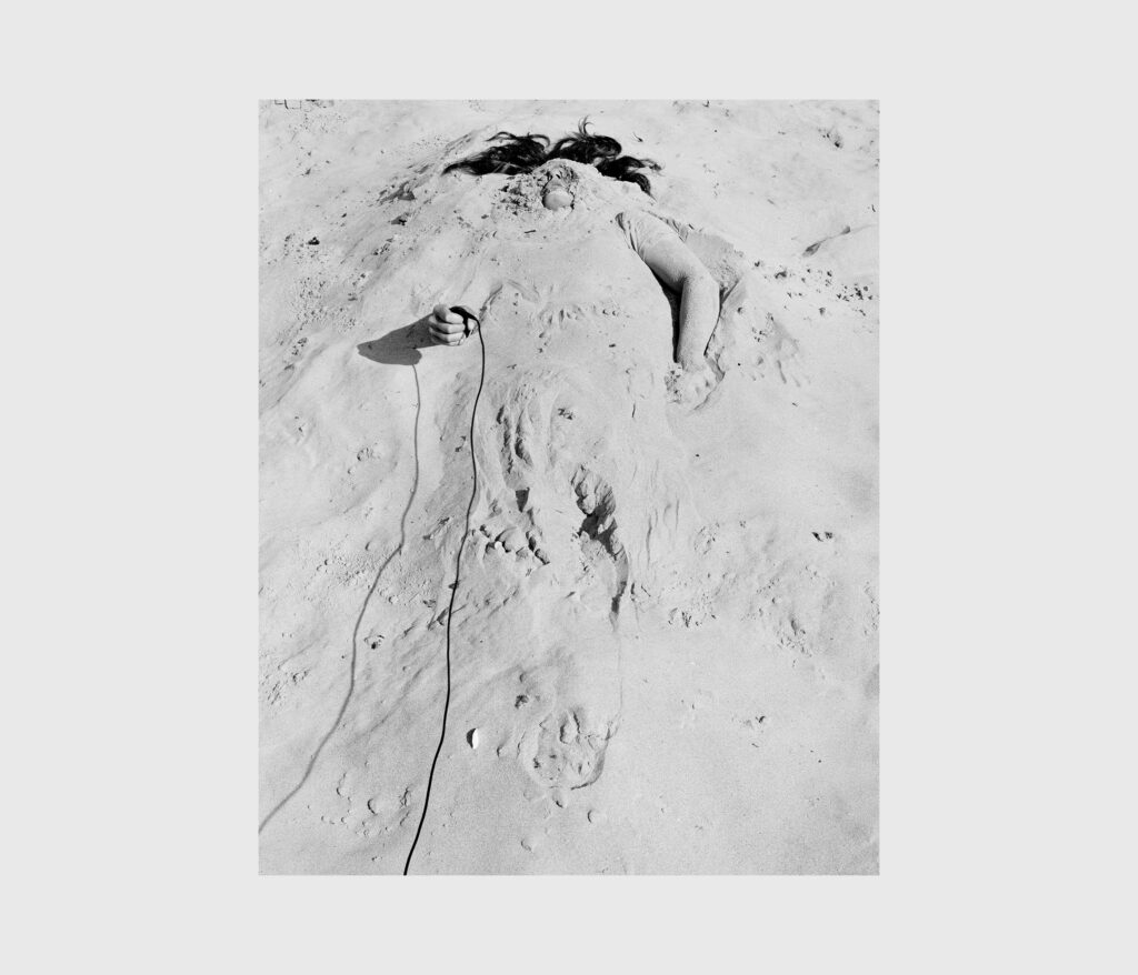 A black and white photo of an individual buried in sand.