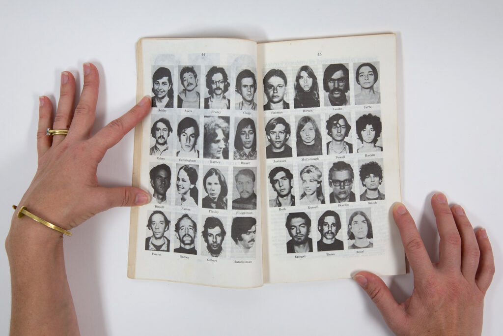 Alice Proujansky, Hard Times are Fighting Times A pair of white hands holds open a book featuring a grid of profiles.