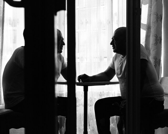 Two men sit across each other at a table.