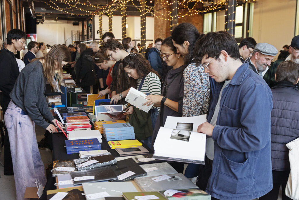 A group of individuals standing around rows of tables looking at books.