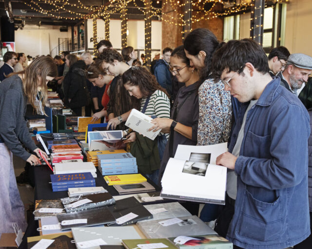 A group of individuals standing around rows of tables looking at books.