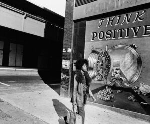 A black woman walks in front of a mural on the street that says "Think Positive"