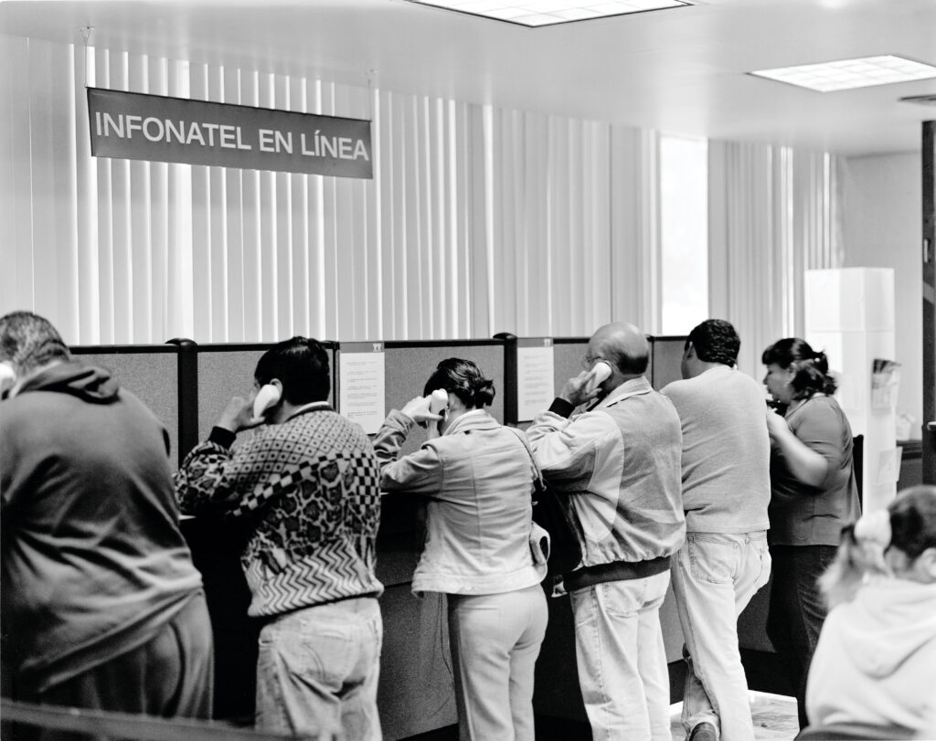 A black and white photo of half a dozen or so individuals facing away from the camera holding phones to their ears.